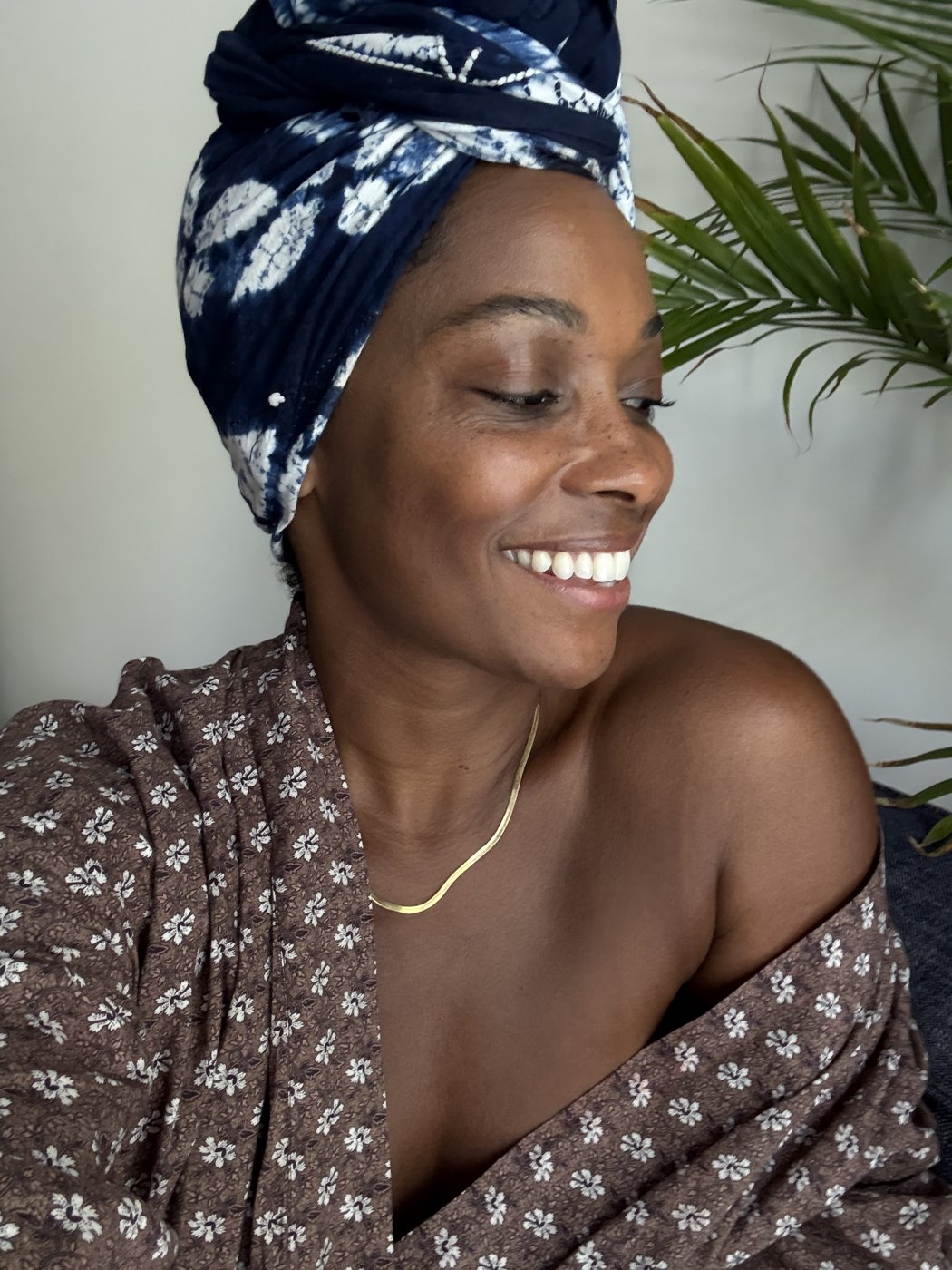 Angela Denae laughing in an indigo head wrap beneath palm fronds.